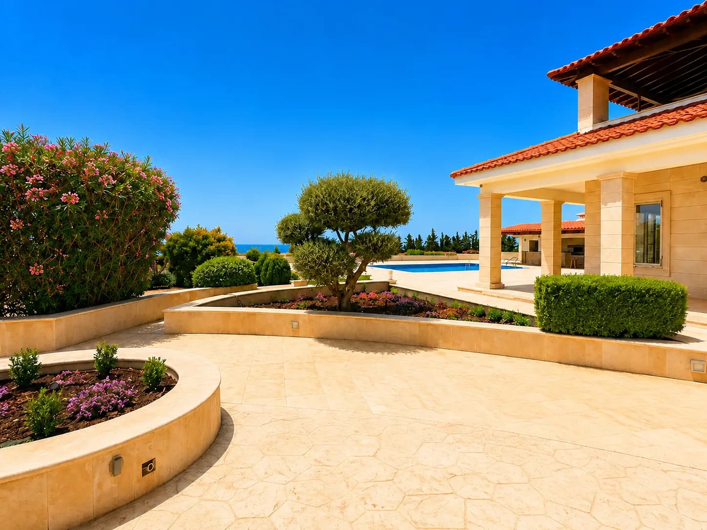 Gartenterrasse der Villa mit blühenden Beeten, einem geformten Baum und Blick über den Pool aufs Mittelmeer.