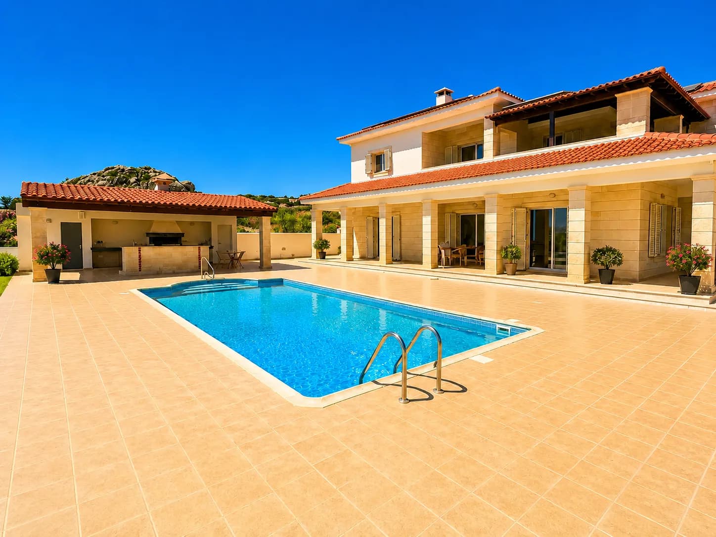 Die MOHANA Villa in Paphos mit großem Pool, Terrasse und überdachter Außenküche unter blauem Himmel.